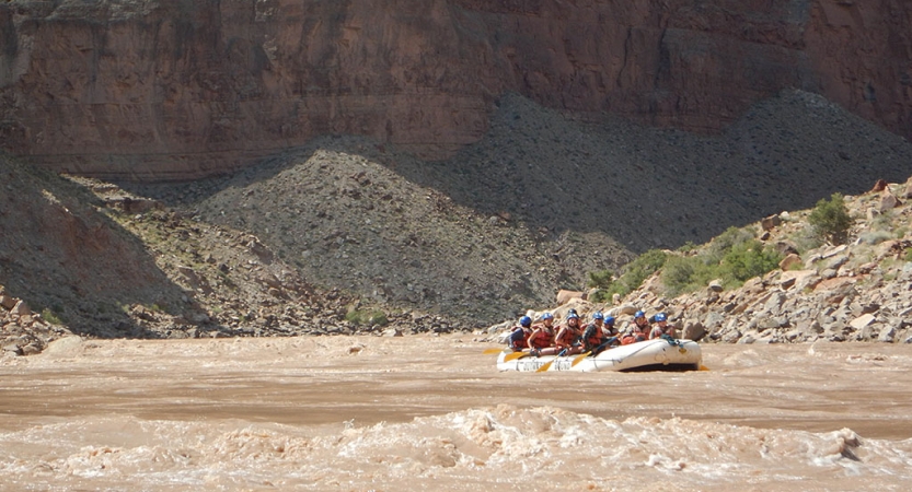 A group of people navigate a raft on a river sided by tall canyon walls