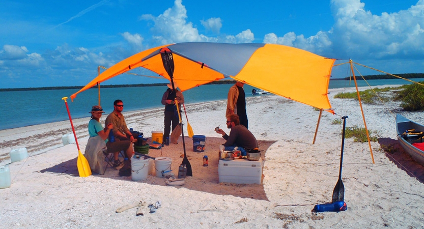 a group of veterans sits under a shelter on a beach during an outward bound course